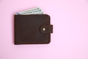 Stylish brown leather wallet with dollar banknotes on pink background, top view. Space for text