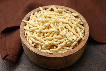 Uncooked trofie pasta in bowl on wooden table, closeup