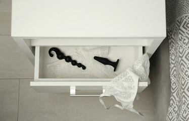 Black anal plug, beads and women's underwear in open drawer of bedside table indoors, above view. Sex toys - obrazy, fototapety, plakaty