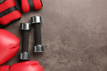 Metal dumbbells, boxing gloves and weights on brown textured table, flat lay. Space for text - obrazy, fototapety, plakaty