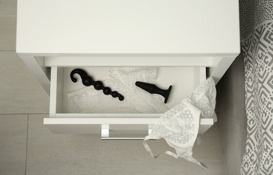 Black anal plug, beads and women's underwear in open drawer of bedside table indoors, above view. Sex toys