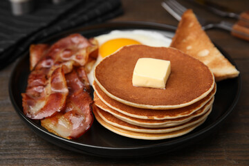 Tasty pancakes served with fried egg and bacon on wooden table, closeup