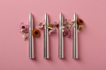Metal bullets and beautiful flowers on pink background, flat lay