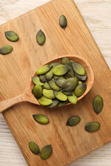 Spoon with pumpkin seeds on wooden table, top view