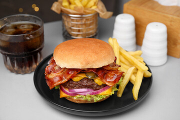Tasty burger with bacon, vegetables and patty served with french fries and glass of refreshing drink on light grey table