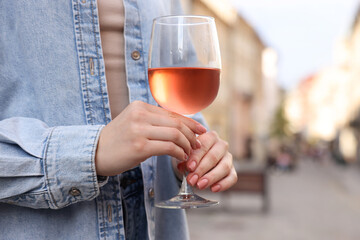 Woman holding glass of rose wine outdoors, closeup. Space for text