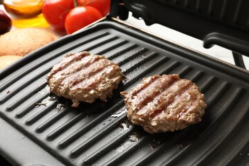 Delicious hamburger patties cooking on electric grill, closeup
