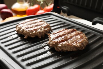Delicious hamburger patties cooking on electric grill, closeup