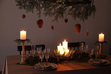 Christmas celebration. Cones hanging from fir tree branch over table with burning candles and tableware