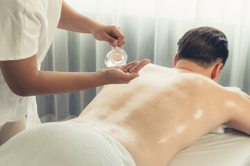 Obraz na płótnie Canvas Masseur hands pouring aroma oil on man back. Masseuse prepare oil massage procedure for customer at spa salon in luxury resort. Aroma oil body massage therapy concept. Quiescent