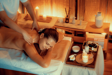 Obraz na płótnie Canvas Caucasian woman customer enjoying relaxing anti-stress spa massage and pampering with beauty skin recreation leisure in warm candle lighting ambient salon spa at luxury resort or hotel. Quiescent