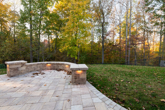 Picturesque backyard view in autumn season with patio pavers and stone wall, autumn leaves, and colorful woods in the background