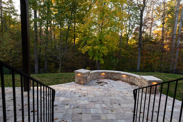 Picturesque backyard view in autumn season with patio pavers and stone wall, autumn leaves, and colorful woods in the background
