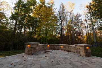 Picturesque backyard view in autumn season with patio pavers and stone wall, autumn leaves, and colorful woods in the background