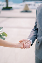 Groom holds bride hand with a bouquet. Cropped. Faceless