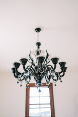 Large black chandelier with white floral decoration hangs on the ceiling opposite the window