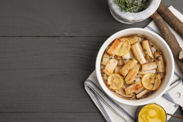 Dish with baked salsify roots, lemon, thyme and sauce on black wooden table, flat lay. Space for text