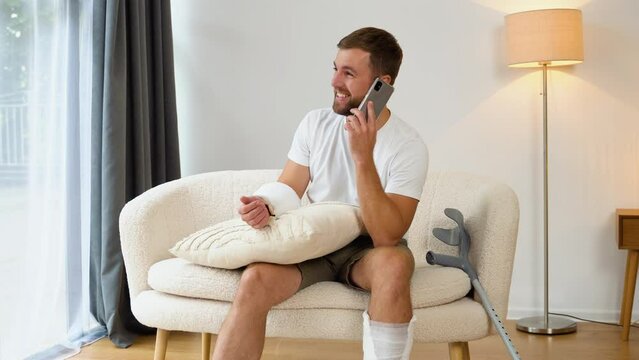A man with broken arm and leg having fun talking on phone with friends during rehabilitation at home