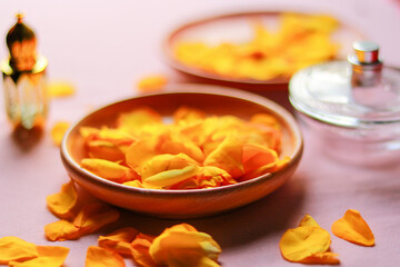 Rose petals in a bowl and a perfume bottle on a pink background.