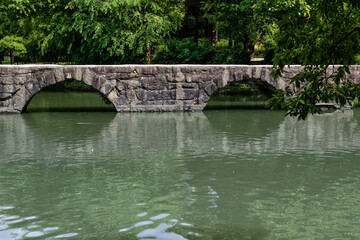 Fototapeta premium An arched stone bridge over a park pond.
