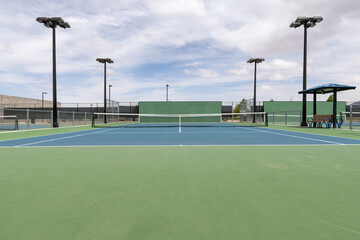 An empty public tennis court during the day with a partly cloudy sky.