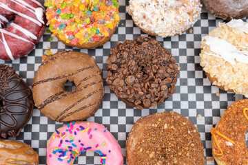 A variety of gourmet donuts arranged on checkerboard pattern paper.