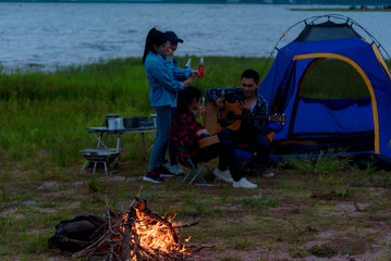 Group of Asian friends camping, relaxing by the sea, mountains Have fun drinking alcohol, partying and singing. Fing the fire in the evening and at night