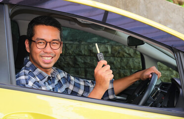 Adult Asian man smiling happy from inside a car while showing the key - obrazy, fototapety, plakaty