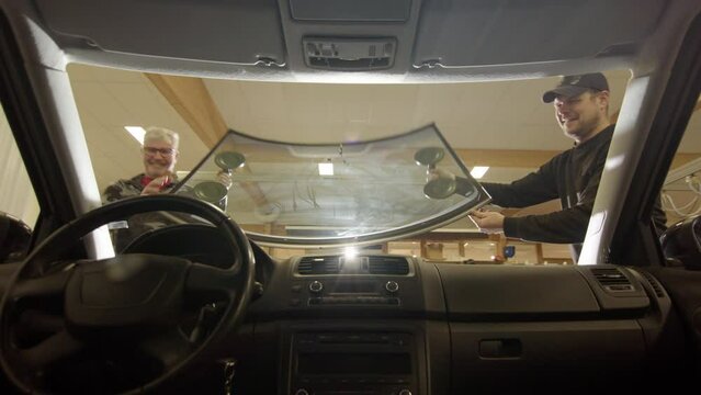 Glass technician repairmen fit new windscreen in place, view from inside car