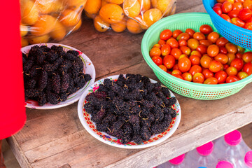 Fresh black mulberry and tomatoes in plastic plates and baskets on a wooden table prepared for sale at the market.