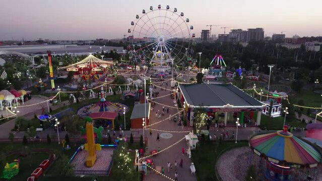 A drone flies over an amusement park with carousels and a Ferris wheel