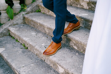 Legs of the groom descending the stairs next to the bride. Cropped. Faceless