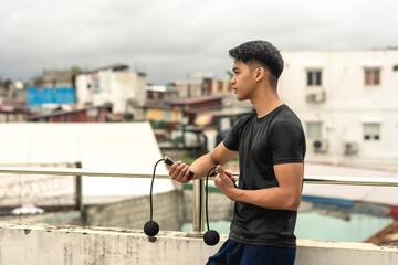 A young handsome asian man holding a cordless jumping ropes outside a floor deck. Cardio training...