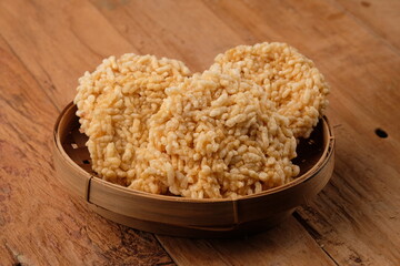 Rengginang is a typical Indonesian snack made from glutinous rice grains that are seasoned and fried. Served on a bamboo container on a wooden table. Indonesian food. Camilan gurih.