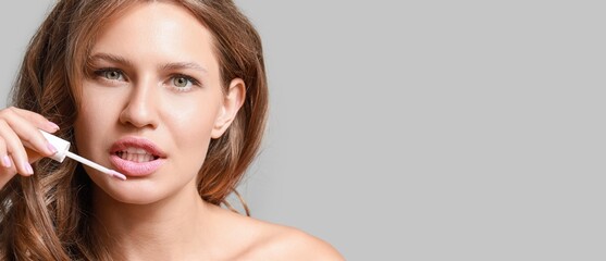 Beautiful young woman applying lipstick against grey background with space for text