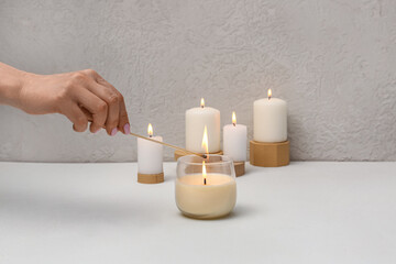 Woman lighting aroma candle on white table
