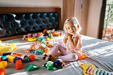 Little girl is sitting on the bed holding a soft toy tightly to her