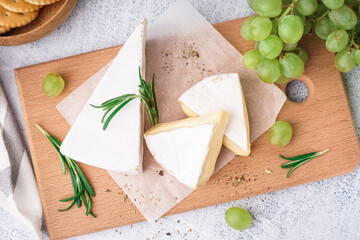 Wooden board with tasty Camembert cheese on light background