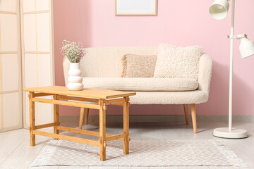 Light wooden coffee table with sofa, dressing screen and floor lamp near pink wall