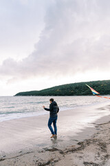 Man with a colorful kite on a rope walks along the sandy beach towards the sea. Side view