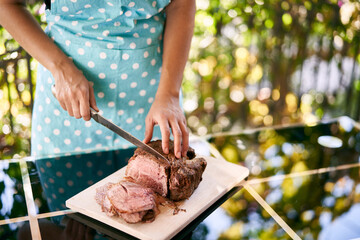 Housewife in an apron cuts slices of roast beef on a mirror table on the balcony