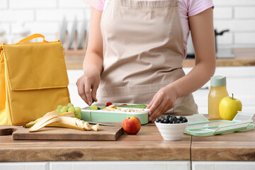 Woman packing fresh meal into lunch box in kitchen