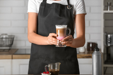 Female barista holding glass cup of tasty coffee in kitchen