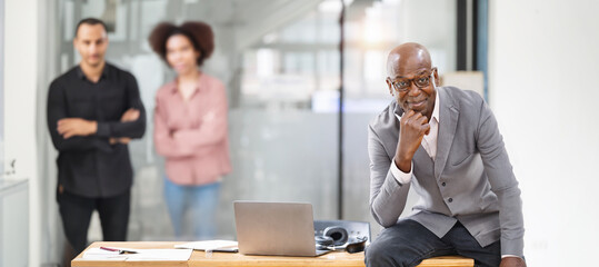Portrait of happy African American small business owner posing in office. Millennial black male team leader smiling, looking at camera, employees team standing in modern office behind.