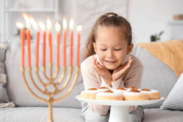 Little girl with donuts celebrating Hanukkah with menorah at home