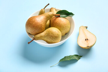 Bowl with ripe pears on blue background