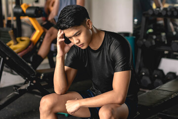 A young handsome asian man feeling disappointed or frustrated while sitting on a bench at the gym. - obrazy, fototapety, plakaty
