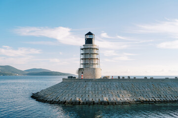 Lighthouse on a breakwater in the sea against the backdrop of a mountain range - obrazy, fototapety, plakaty