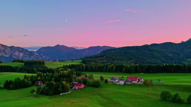Panoramic shot of a land with trees and few houses visible mountains in the distance with pink sky 
