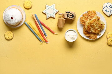 Hannukah composition with potato pancakes, candles, sour cream and dreidels on yellow table